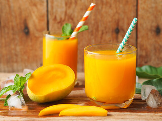 Mango juice with fresh ripe mango sliced on a rustic wooden table for summer drinks concept.
