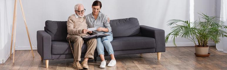 adult woman and aged father looking at family photos while sitting on sofa at home, banner