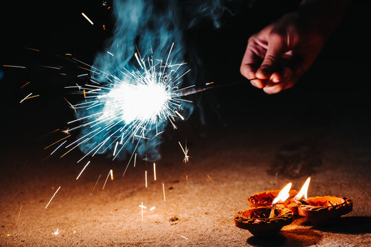 Female hand holding sparklers and Diya in background during celebration of Diwali festival in India