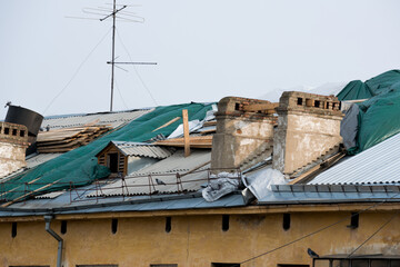 Fototapeta na wymiar Roof repairs of an apartment building. The roof collapsed under the weight of snow. Damaged falling roof and chimney on sunny day with clear blue sky.