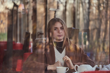 Slightly blurry portrait of a charming girl, made through the window of a cafe. The window reflects the autumn Park.