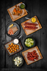 Laid table for a company with an assortment of dishes: fried sausages, dumplings, shrimps, fried chicken necks and fish backs. Festive table with delicious food.