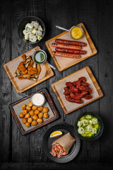 Laid table for a company with an assortment of dishes: fried sausages, dumplings, shrimps, fried chicken necks and fish backs. Festive table with delicious food.