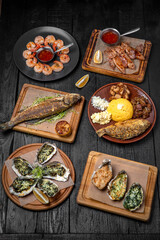 Fish and seafood dishes: oysters, trout, squid, shrimp. Several dishes on a background of black boards. Festive table with delicious food.