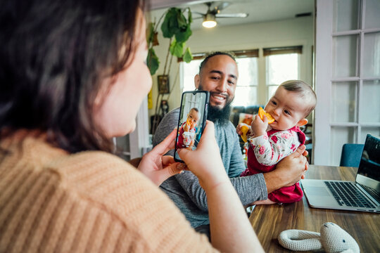 Mom taking cell phone photo of dad holding baby eating orange