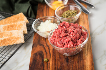Gourmet Rindertatar Beef Tatar  aus Rindfleisch Filet fettarm  und roh, Kapern, Eigelb, Zwiebeln, Toast Brot auf Holzbrett und Marmor Hintergrund hell