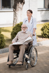social worker walking with handicapped man holding newspaper in wheelchair