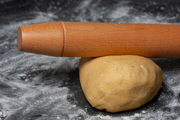 Raw Cookie dough on a slate plate which is covered with flour. A rolling pin is lying on top.