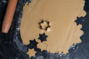 Raw Cookie dough on a slate plate. Some are already cut out in a Starshape, a rolling pin is lying on the side and the plate is covered with flour.