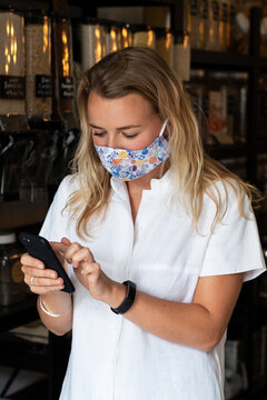 Woman wearing face mask shopping in waste-free local store, using a phone