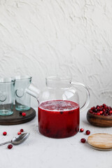Cranberry juice in a glass transparent teapot on a concrete background. Berry cold drink. Making homemade lemonade.