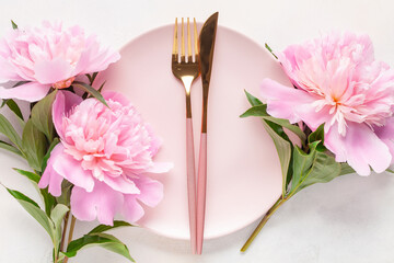 Pink peony flowers and a plate with cutlery on the table. Top view. Flat lay