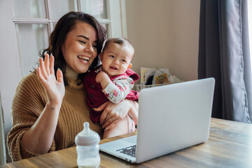 Mother doing video chat with baby on laptop computer at dining room table 
