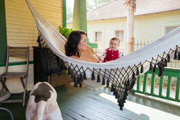 Mother playing with baby in hammock on front porch of home