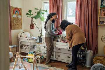 Mother and father dressing baby together in nursery room