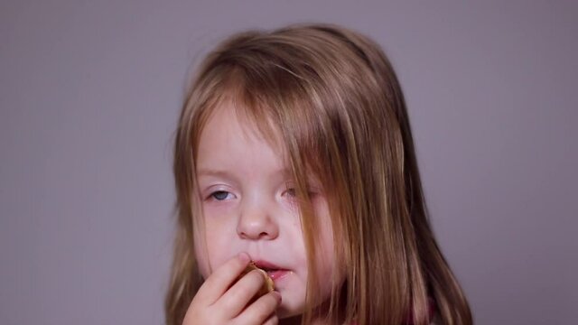 pretty little blonde girl eats a cookie and drinks juice on greyish background. Full HD footage