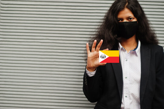 Asian woman at formal wear and black protect face mask hold Marquesas Islands flag at hand against gray background. Coronavirus at country concept.