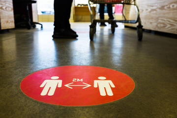 Red round sign printed on ground at supermarket cash desk register informing people to keep 2 meter...
