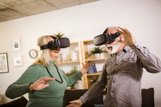 Senior couple play virtual reality glasses headset playing video game and have fun together in living room at home.