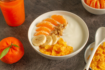Tasty tangerine smoothie bowl with fruits, cereals, seeds and turmeric powder over grey background from above