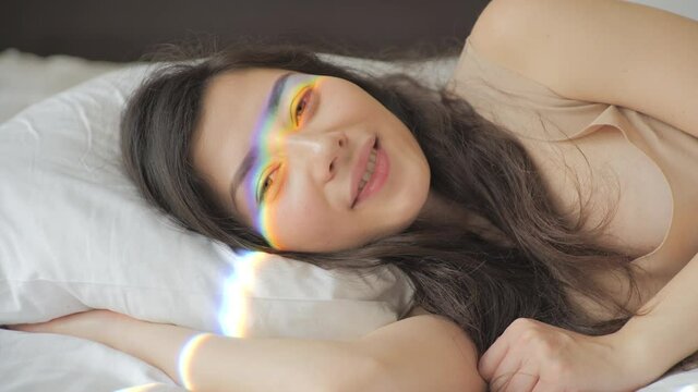 Happy girl meets a new day. Pretty mixed race woman waking up and smiling in the morning. Rainbow flare on her face. Sun shining bright. Beauty and happiness concept.