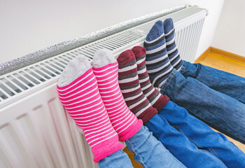 A family in bright warm winter socks warms their feet on the heating radiator in the house....