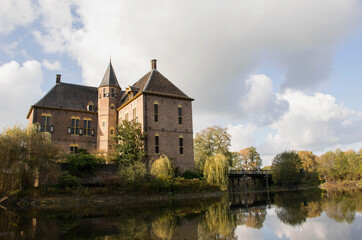 Fototapeta na wymiar Dutch medieval castle in autumn landscape with moat and fall trees. Castle reflection in water. Dramatic afternoon light. Travel destination gelderland, the netherlands. Heritage buildings. 
