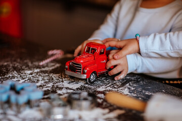 Child's hand playing with red toy car on a kitchen table with a flour. Christmas.