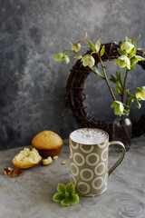 Frothy coffee in a large ceramic cup. A minimalistic photo with a drink and flowers.