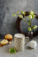 Frothy coffee in a large ceramic cup. A minimalistic photo with a drink and flowers.