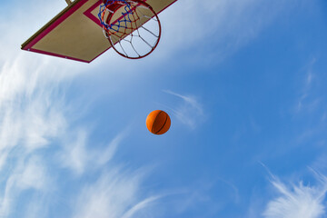 A basketball ball flies into a hoop with a net against a blue cloudy sky. Sports activities on the playground.