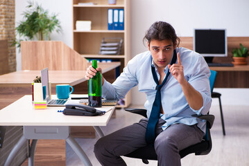 Young male employee drinking alcohol at workplace