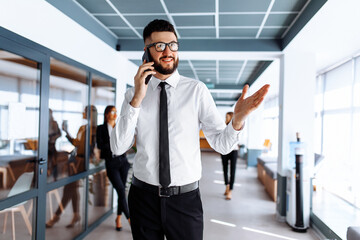 Happy young business man talking on cell phone in office