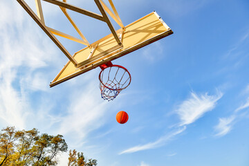 Flying basketball ball in the hoop on the background of the cloudy sky. Sports activities on the playground. © andov