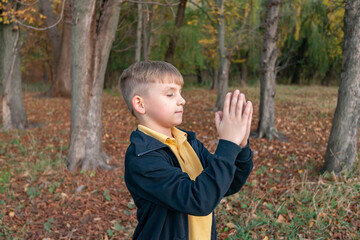 The boy clasped his hands together and offers prayer to God in the open air park.