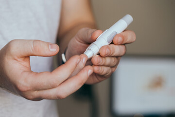 Medicine, diabetes, glycemia, healthcare and people concept - close up of a man's hands using a lancet on his finger to check blood glucose meter with copy space for text