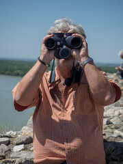 Senior caucasian man looking through binoculars and observe landscape.