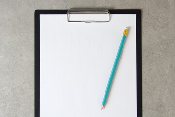 Template of white paper with simple pencil on light grey concrete background in a black tablet with a clip. Concept of new idea, business plan and strategy,  empty space for text