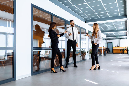 Group of attractive business people standing and communicating together, holding cups, in a modern office. Coffee break.