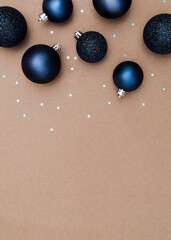 Classic navy blue Christmas baubles against a plain natural brown paper background. Flat lay style portrait image with blue sparkle stars and glitter decorations. Copy space available.