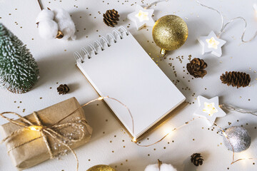 Christmas festive decorations and notebook. With wish list and 2021 goals concept. Notebook mock up, gift, and coton branch with shiny golden balls.New year flat lay, top view, copy space..