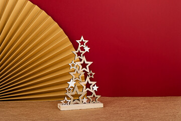 Closeup of a decorative Christmas tree made of golden stars with a paper fan on red background. Stylish modern Xmas decorations
