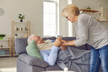 Obraz premium Cheerful laughing senior woman looks happy giving a sick beloved aged man a glass of water