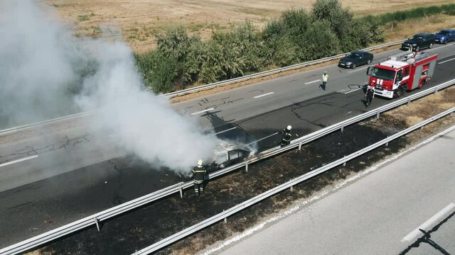 Firefighters extinguish burning car on highway following a serious car accident on hot summer day aerial view. Fire truck came to the rescue. The flow of cars on the track. Problem is on the road.