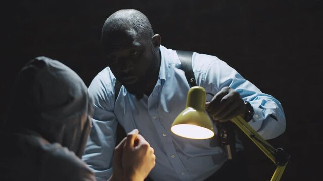 African officer interrogating man suspected of crime glowing light of lamp into face