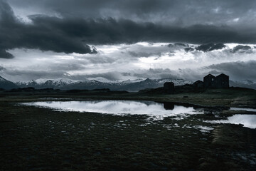 Dramatic weather over Icelandic farm ruins at dusk reflected in flooded field
