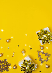 Christmas background. White gifts with golden bow, yellow balls and sparkling lights in xmas decoration on yellow background for greeting card. Decoration and copy space for your text.