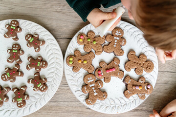 Horizontal detail of unrecognizable children decorating ginger cookies in the kitchen. Christmas recipe of traditional sweet chocolate desserts for the festivities. Lifestyle with kids at home.