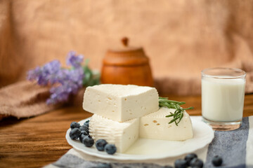 A glass of goat milk and a head of goat milk cheese stand on a wooden table. Cheese at home.