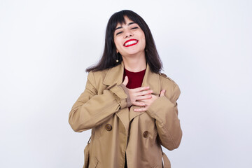 Beautiful young Caucasian woman standing against white background smiling with hands on chest with closed eyes and grateful gesture on face. Health concept. 
